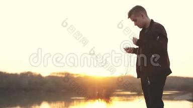 年轻的帅哥戴着耳机在日落时在海滩上听音乐。 慢动作。